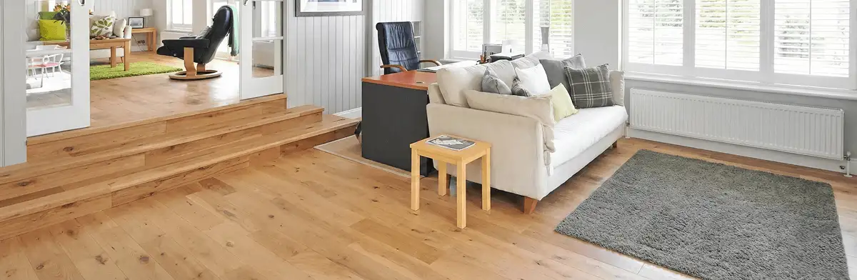 A modern living room with professionally installed laminate flooring, a beige sofa, a small side table, a gray rug, and large windows with white shutters in Henderson, NV